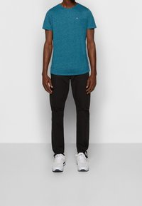 Tyrkysové tričko s krátkým rukávem a kulatým výstřihem, s malým logem na hrudi, spárované s černými cargo kalhotami a bílými sportovními teniskami.