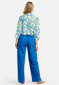 Long-sleeve shirt with a white base, blue and green abstract floral pattern. Paired with high-waisted, loose-fitting blue pants.