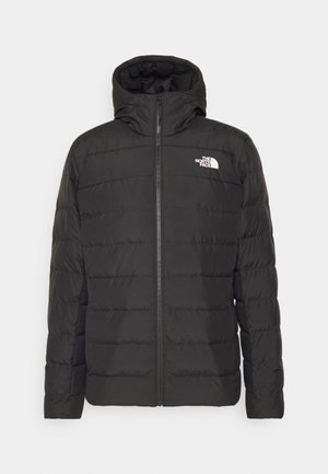 Doudoune noire avec capuche, fermeture éclair à l'avant et design matelassé. Elle arbore un logo sur la poitrine gauche et des poignets élastiques pour un ajustement confortable.