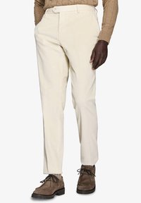 Pantaloni in corduroy crema con una vestibilità dritta, caratterizzati da una trama a coste visibili, tasche laterali e cintura con passanti. Combinati con scarpe marroni.
