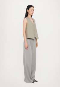 Lys grå ermeløs topp med V-hals og tre knapper, kombinert med vide grå bukser. Glatt stoff med minimalistisk design.