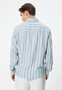 Camisa de manga larga a rayas azul y blanca, hecha de tejido ligero, con detalle de yugo en la parte trasera y puños abotonados.