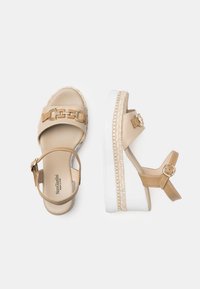 Sandali platform beige con una texture liscia, catena decorativa dorata e cinturino regolabile. Presentano una suola bianca con dettagli intrecciati.