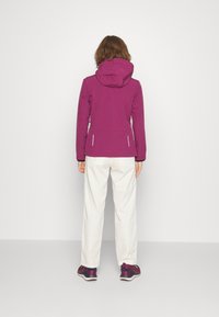 Fuksjowa wodoodporna kurtka z kapturem, dopasowany fason i kieszenie na zamek, noszona z białymi spodniami i ciemnymi trampkami. Gładka faktura.