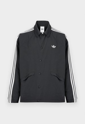 Crna sportska jakna s kopčanjem na gumbe, bijeli troprugasti dizajn na rukavima i mali bijeli logo na prsima. Teksturirana tkanina.