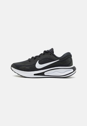 Chaussure de running Nike noire et blanche avec tige en mesh, fermeture à lacets, semelle épaisse et rembourrée, et logo Nike blanc très visible sur le côté.