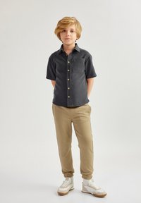 Sort kortærmet skjorte med en brystlomme og knapdetalje, parret med tan farvede tapered sweatpants og hvide sneakers med strukturerede accenter.