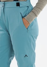 Ljusblå utomhusbyxor med en ficka med dragkedja, justerbart midjeband och logotypdetalj på låret. Slätt, hållbart tyg.