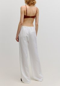 Braunes Crop-Top mit dünnen Trägern und goldenen Akzenten, kombiniert mit lockeren weißen Hosen, die einen elastischen Bund und eine Gesäßtasche haben.