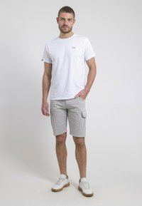 T-shirt en coton blanc avec un petit logo sur la poitrine gauche, associé à un short cargo gris clair avec des poches latérales, et des baskets blanches.