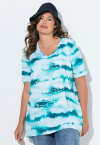 Camisa de tirantes en teñido anudado turquesa con escote en V, que presenta un gráfico de pez blanco. Tejido suave con un ajuste holgado, combinada con pantalones cortos de mezclilla.