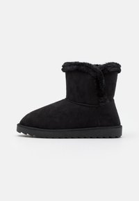 Zwarte enkelboot gemaakt van zacht suede materiaal, met een nepbontafwerking op de kraag, ronde neus en een geaccentueerde rubberen zool.