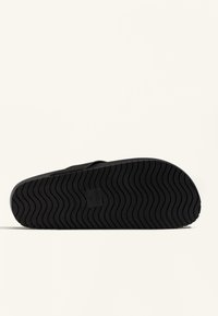 Talpa din cauciuc negru pentru sandale, cu un model de profil ondulat, având un logo dreptunghiular pe arcul piciorului. Designul este simplu și funcțional.