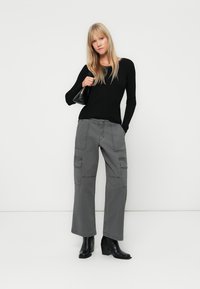 Top negru cu maneci lungi și nervuri, asortat cu pantaloni cargo gri cu picioare largi, care prezintă buzunare laterale și detalii cusute, completat cu botine negre.