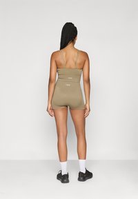 Ελαιόχρωμο αθλητικό ρουχισμό με εφαρμοστή σχεδίαση, λεπτούς διπλούς ιμάντες και λεπτομέρεια λογότυπου στο πίσω μέρος. Κοντά πόδια και απαλό υλικό.