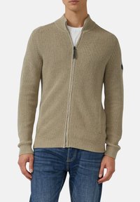 Beige gestrickte Strickjacke mit hohem Kragen, Reißverschluss und gerippter Textur. Verfügt über zwei seitliche Taschen und ein figurbetontes Design.