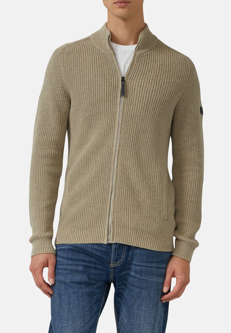Beige gestrickte Strickjacke mit hohem Kragen, Reißverschluss und gerippter Textur. Verfügt über zwei seitliche Taschen und ein figurbetontes Design.