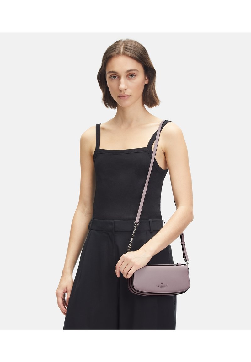 Mała prostokątna torebka w jasnofioletowej skórze, z srebrnym łańcuszkiem, gładką fakturą i detalem logo z przodu.