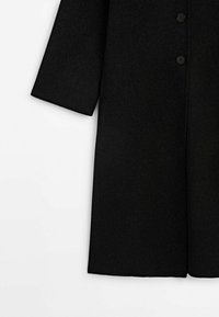 Manteau en laine noire à manches longues avec deux boutons visibles, présenté de la taille à l'ourlet sur fond blanc.