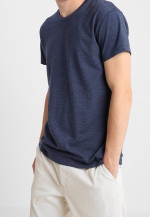 Navy blue crew neck t-shirt made of soft fabric, featuring short sleeves and a relaxed fit, paired with light-colored pants.