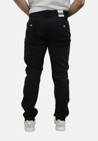 Zwarte denim jeans met een slim fit, voorzien van achterzakken, gouden hardware-accenten en een label op de tailleband. Draagt met witte sneakers.