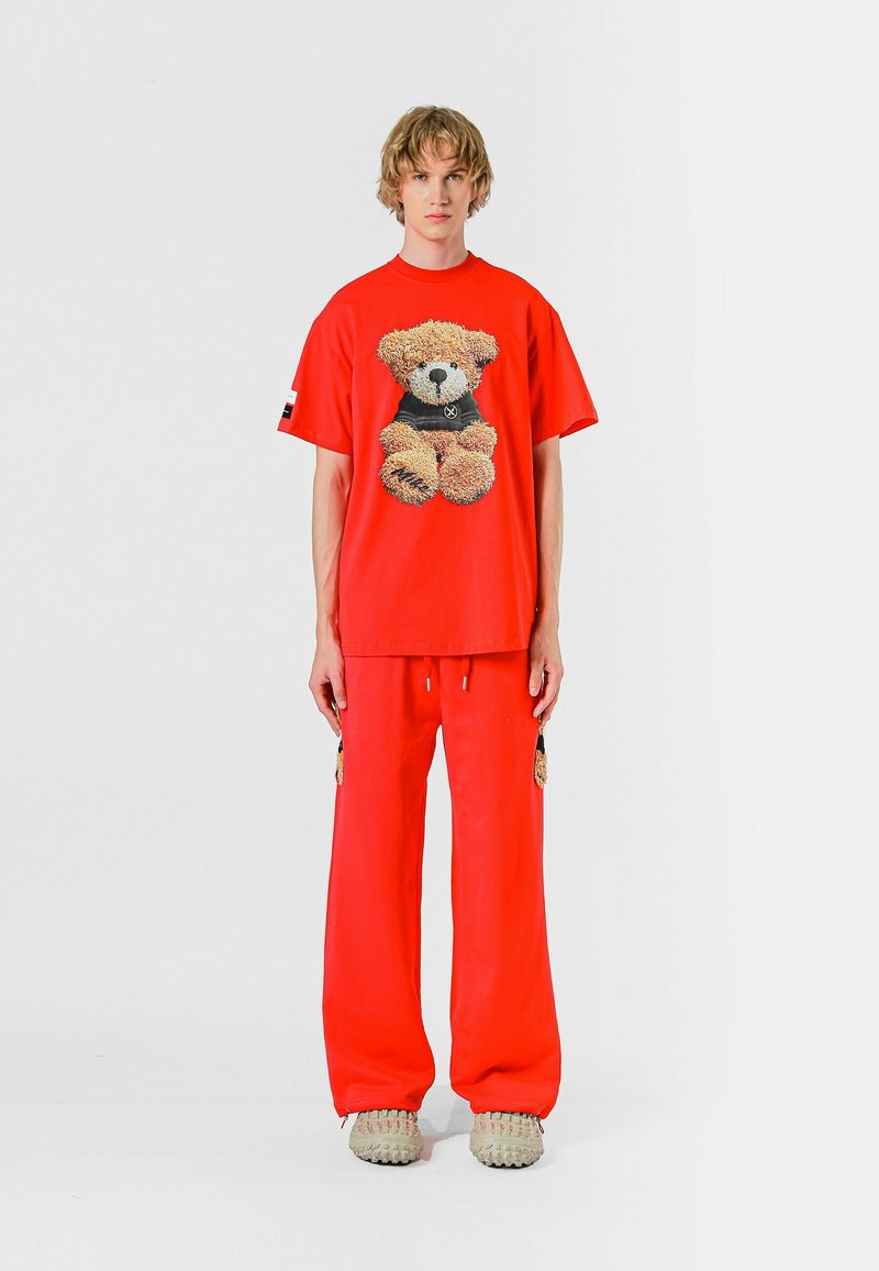 Camiseta de algodón roja con un gráfico de oso de peluche, combinada con pantalones de chándal rojos a juego. Tejido texturizado y diseño de corte holgado. Calzado casual.