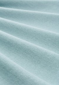 Helles blaues Gewebe mit glatter Textur und sichtbarem Webmuster, das sanfte Falten und subtile Schattierungen zeigt.