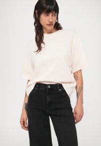 Camiseta rosa claro de gran tamaño hecha de tela suave, con escote redondo y mangas cortas, combinada con jeans negros de cintura alta.