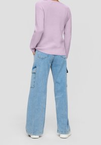 Pull en maille côtelée lilas à manches longues, associé à un jean cargo bleu ample avec poches latérales et coupe décontractée. Des baskets blanches complètent le look.