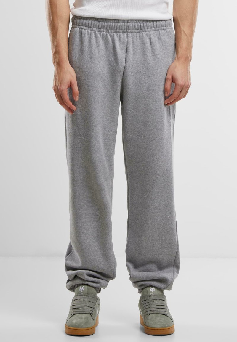 Un pantalon de jogging gris avec une taille élastique, des poches latérales et une coupe fuselée à la cheville, associé à des chaussures de sport grises.