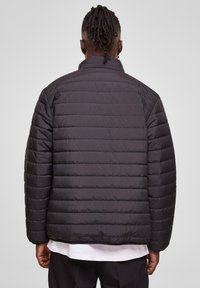 Black quilted jacket with a stand collar, featuring horizontal stitching, ribbed cuffs, and a relaxed fit. Smooth, slightly shiny material.
