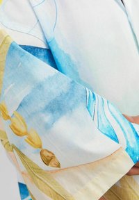 Tessuto leggero e colorato con un design astratto blu e giallo impreziosito da elementi floreali. Texture morbida con una forma che cade.