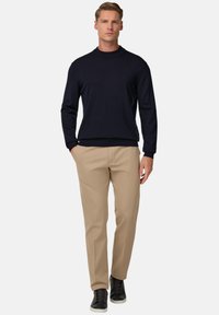 Navy knit sweater with a high neckline, paired with beige trousers and black low-top sneakers. Simple design, smooth texture, tailored fit.