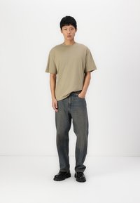 Fitted beige cotton t-shirt, relaxed-fit blue denim jeans, and black slip-on shoes. Simple design with no visible patterns or logos.