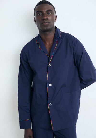 Chemise de pyjama bleu marine à boutons avec des détails colorés le long du col et à l'avant. Confectionnée en tissu lisse, elle comporte deux poches avant.