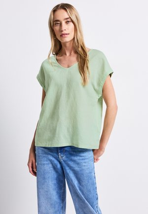 Haut vert clair à manches courtes avec un col en V, coupe décontractée et texture douce. Porté avec un jean bleu ample.