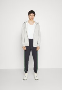 Gray zip-up hoodie with white interior, paired with black joggers featuring green side stripes. Model wearing white sneakers.