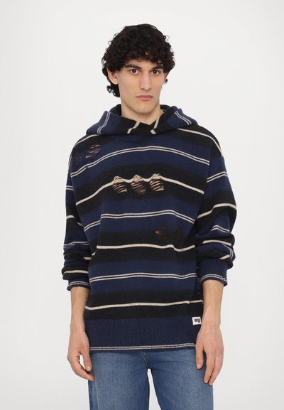 Hoodie rayé bleu marine et noir avec une détresse visible, présentant une grande capuche et des poignets côtelés. Rayures beige accentuées notables.