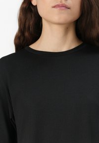 Zwarte langemouwen t-shirt met een ronde hals, gemaakt van zachte stof met een gladde textuur, getoond van de borst omhoog.