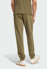 Person wearing olive green ribbed shirt and matching jogger pants with white sneakers with orange details, viewed from behind.