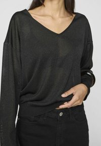 Mustat, kevyet neuleet, joissa on V-pääntie, pitkät hihat ja rento istuvuus. Hieman läpikuultava rakenne, yhdistettynä mustiin korkeavyötäröisiin farkkuihin.