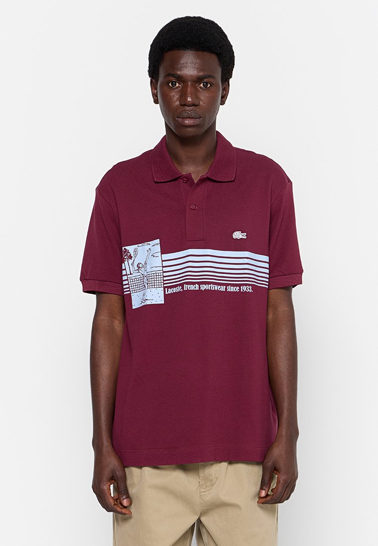 Burgundowa koszulka polo z żebrowanym kołnierzykiem, z graficznym panelem z niebieskimi paskami i napisem "Lacoste, francuska odzież sportowa od 1933 roku."