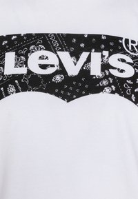 Hvit t-skjorte med et svart og hvitt bandana-mønster, hvor "Levi's"-teksten er tydelig vist i fete hvite bokstaver.