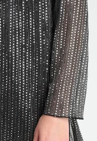 Sort og gennemsigtig langærmet kjole med lodrette striber og sølvglitrende pailletdetaljer, der forbedrer teksturen og tilfører visuel interesse.