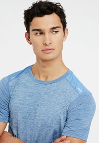 Modrá športová tričko s textúrovanou látkou, krátkymi rukávmi a kontrastnými ramenami. Ľahký a priedušný dizajn.