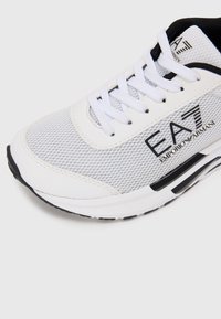 Bijele mrežaste tenisice s crnim akcentima, s udobnom potplatnom i teksturiranim dizajnom. Brend logo "EA7 Emporio Armani" sa strane.