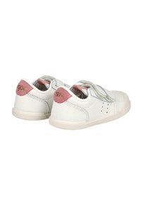 Zapatitos blancos para niños pequeños con acentos de talón rosa, correas de velcro y "1974" impreso en la parte trasera del talón, mostrados desde ángulos trasero y lateral.