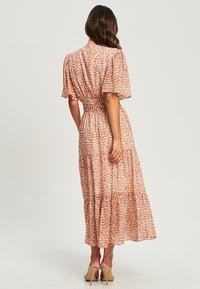 Maximekko kevyestä, kuvioidusta kankaasta, jossa on kireä vyötärö, lyhyet puffihihat ja kerrostettu helma vaaleanpunaisen ja kermaisen sävyissä.