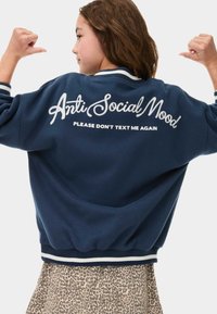 Sweatshirt bleu marine avec texte brodé blanc au dos indiquant "Humeur Anti Sociale, Merci de Ne Pas Me Textoter Encore." Présente des poignets rayés.