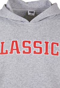 Grijze hoodie van katoen met een grote, rode, geborduurde "CLASSIC" tekst aan de voorkant. Voorzien van een capuchon met trekkoord en een zachte textuur.